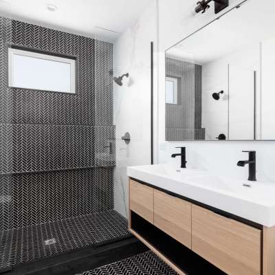 A beautifully renovated bathroom with a wood vanity cabinet, black marble herringbone tiles in the shower, and a white countertop with black faucets.